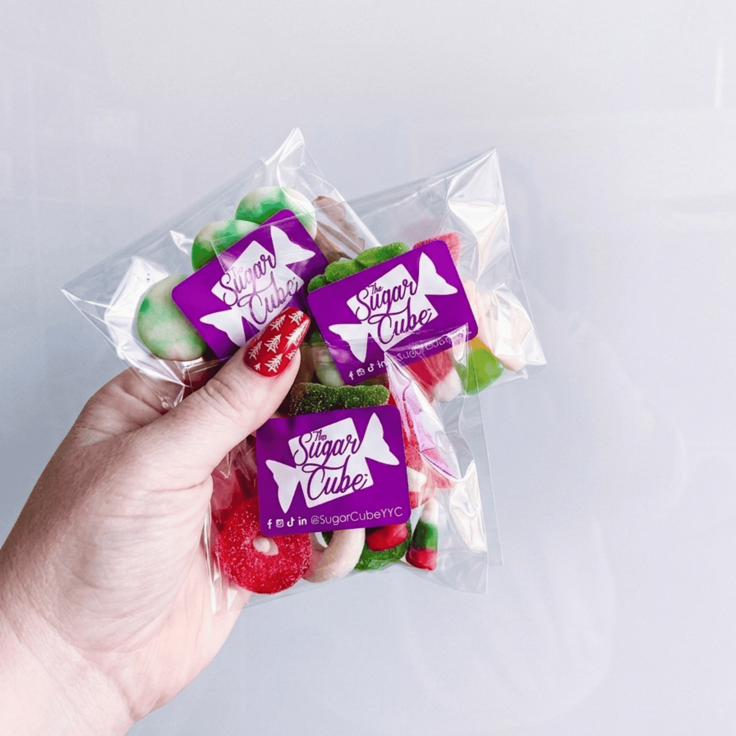 Hand holding three Spread the Cheer Christmas candy bags to show the size of the approximately 50g candy bags