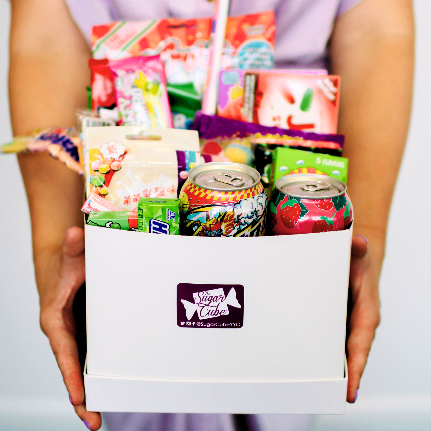 Holding a Large candy gift basket for size with approximately 15 to 20 assorted treats, including specialty soda bottles and cans